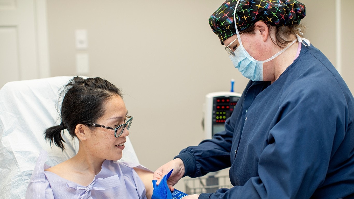 Smiling woman in white blouse against gray wall.