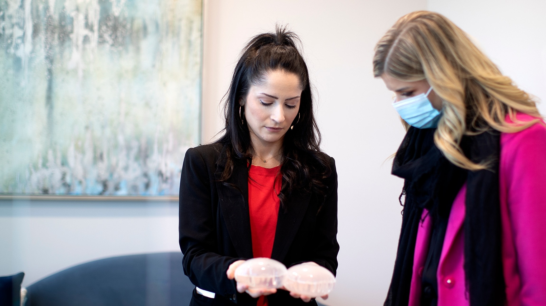 Women examining breast implant models indoors.